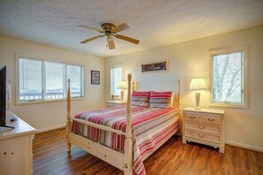 Ein Schlafzimmer mit Himmelbett, Deckenventilator, Nachttischlampen, einem Nachttisch, einer Kommode und einem an der Wand befestigten Schild.