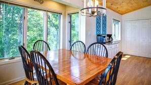 A dining area with a wooden table and chairs, large windows, and a kitchen with white cabinets. - Blue Mountain Breeze with multi-mountain range vie (Blowing Rock)