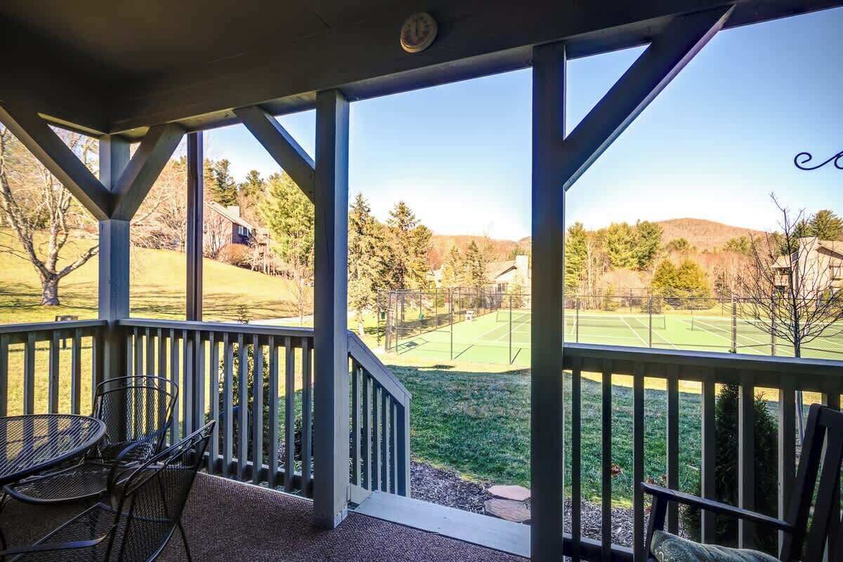 A covered outdoor area with a view of a green field and trees.