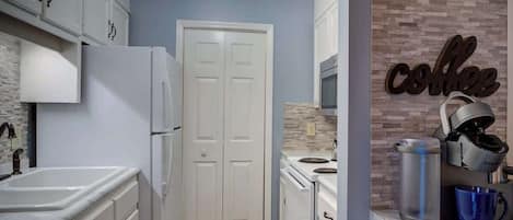 A compact kitchen with white cabinets, a double-door refrigerator, a microwave, and a coffee machine.