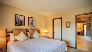 Une chambre à coucher avec un grand lit, deux tables de chevet, une porte et des œuvres d’art encadrées accrochées au mur.