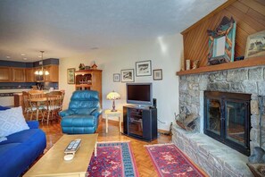 A living room with a fireplace, a television, a blue sofa, and a dining area with wooden furniture. - Chetola Juniper #8 is a beautiful one bedroom cond (Blowing Rock)