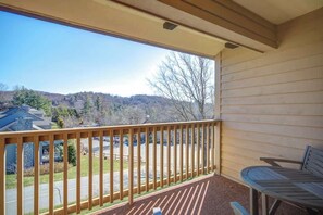A balcony with a wooden railing, a bench, and a view of a parking lot and buildings. - Chetola Juniper #8 is a beautiful one bedroom cond (Blowing Rock)