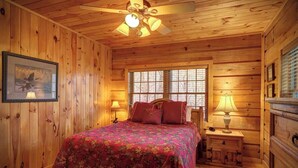 A wooden cabin bedroom with a bed, two bedside lamps, a ceiling fan, and a window. - Arbor Den Log Cabin 3 Bedroom, 3 Bath, Pet friendly (Blowing Rock)