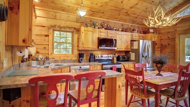 A wooden cabin interior with a kitchen, dining area, and a large window. - Arbor Den Log Cabin 3 Bedroom, 3 Bath, Pet friendly (Blowing Rock)