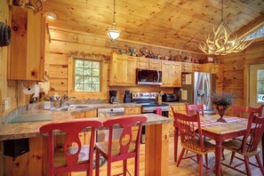 A wooden cabin interior with a kitchen, dining area, and a large window. - Arbor Den Log Cabin 3 Bedroom, 3 Bath, Pet friendly (Blowing Rock)