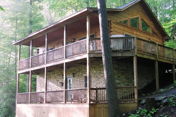 Une cabane en bois à deux étages, dotée d’un balcon au niveau supérieur et entourée d’arbres.