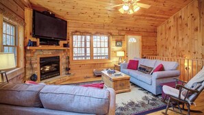 A log cabin interior with a fireplace, television, and seating area. - Arbor Den Log Cabin 3 Bedroom, 3 Bath, Pet friendly (Blowing Rock)