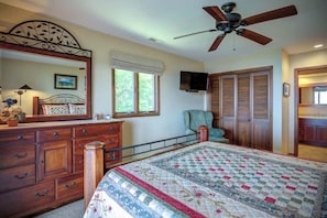 Quarto com cama, penteadeira, espelho, televisão e ventoinha no teto.