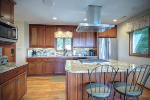 A modern kitchen with wooden cabinets, a stainless steel range hood, and a central island with bar stools. - Blissful Vista has breathtaking gorge views, seclu (Blowing Rock)