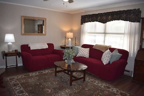 A living room with two red sofas, a wooden coffee table, a patterned rug, a mirror, and a window with curtains. - Minute to Main - Steps to Main St Blowing Rock (Blowing Rock)
