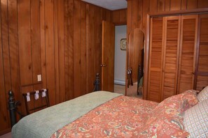 A bedroom with wooden paneling, a bed with patterned bedding, a chair, and a wardrobe. - Minute to Main - Steps to Main St Blowing Rock (Blowing Rock)