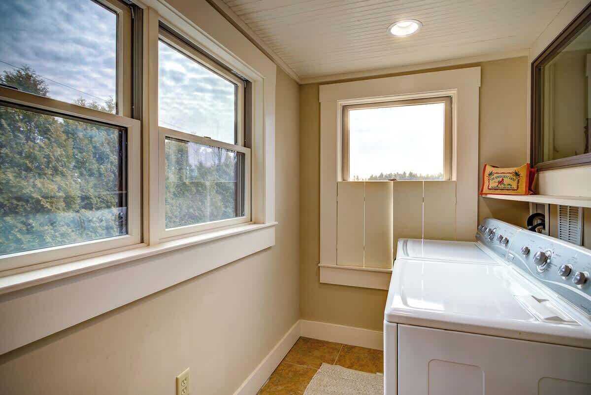 A laundry room with a washer and dryer, large windows, and a view of trees.