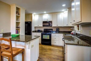 A kitchen with white cabinets, a black refrigerator, a microwave, a stove, and a green bowl on the counter. - The Hill is the best in country living, minutes fr (Blowing Rock)