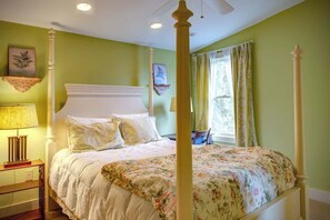 Un letto a baldacchino con copripiumino floreale, un comodino con lampada e una finestra con tende.