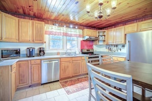 A kitchen with wooden cabinets, a stainless steel refrigerator, a dishwasher, and a dining area with a table and chairs. - Uli's Place - Charming spot near the Parkway! (Blowing Rock)