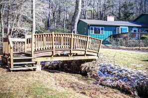 Un pont de fusta sobre un rierol que condueix a una casa amb façana blava.