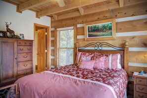 Une chambre à coucher de style cabane en bois, avec un lit, une commode et un tableau accroché au mur.