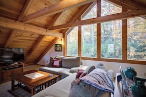 A cozy loft bedroom with a large window, wooden beams, a television, and a sofa. - Ollie's Overlook  fabulous multi-level cabin locat (Lenoir)