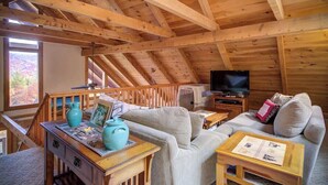 Um interior em madeira com televisão, sofá e uma mesa com um vaso e moldura de quadro.