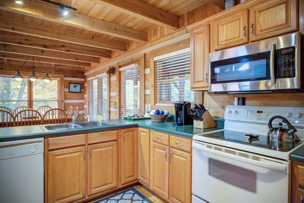 A kitchen with wooden cabinets, a stainless steel microwave, a white stove, and a sink.