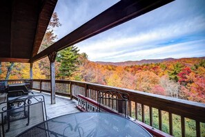 Eine überdachte Terrasse mit Tisch und Stühlen, mit Blick auf einen Wald im Herbstlaub.