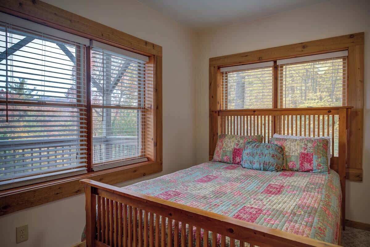 Een slaapkamer met een houten bedframe, een gewatteerde spreidek en een raam met jaloezieën.