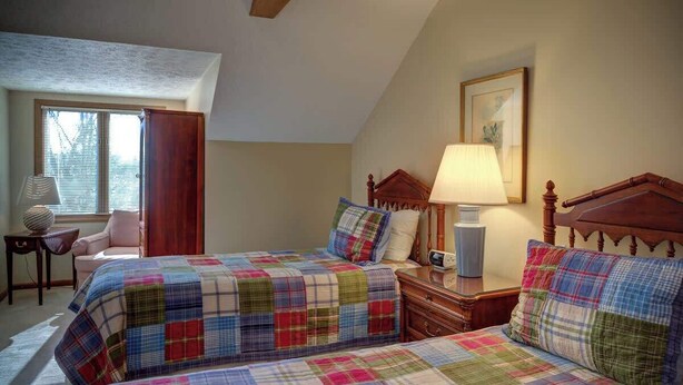 A bedroom with two beds, a bedside table, a lamp, a chair, and a window with blinds. - One Level Entry 3 bed 3 bath condo at Chetola (Blowing Rock)