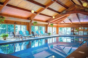Uma grande piscina interior com espreguiçadeiras e teto de madeira.