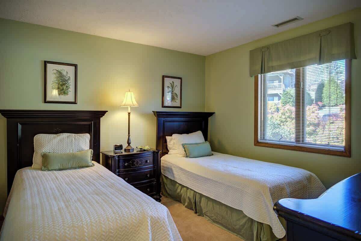A room with two beds, a nightstand, a lamp, and a window with blinds.