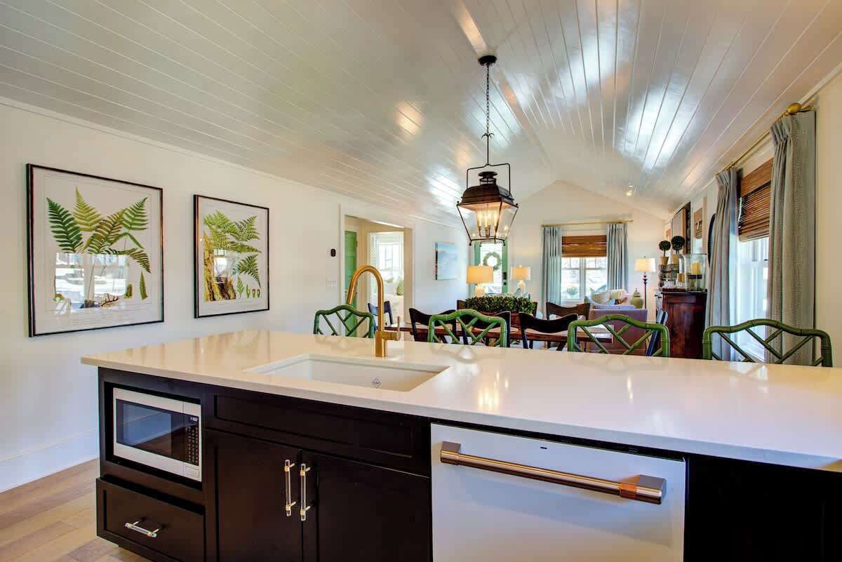 A modern kitchen with a large island, built-in appliances, and a dining area with green chairs.