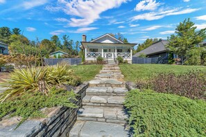 A house with a stone pathway leading to a porch, surrounded by greenery and other houses. - Little House on Main in Downtown Blowing Rock (Blowing Rock)