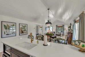 A spacious kitchen with a central island, a dining area with a table and chairs, and a view of the outdoors through a window. - Little House on Main in Downtown Blowing Rock (Blowing Rock)