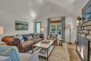 A living room with a leather sofa, a coffee table, a side table, a fireplace, and a painting on the wall. - Little House on Main in Downtown Blowing Rock (Blowing Rock)