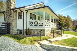 Ein modernes Haus mit einem Steinsschornstein, einer überdachten Veranda mit Geländer und einer Auffahrt mit Kies.