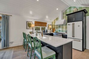 A modern kitchen with a central island, green chairs, a stove, and a refrigerator. - Little House on Main in Downtown Blowing Rock (Blowing Rock)