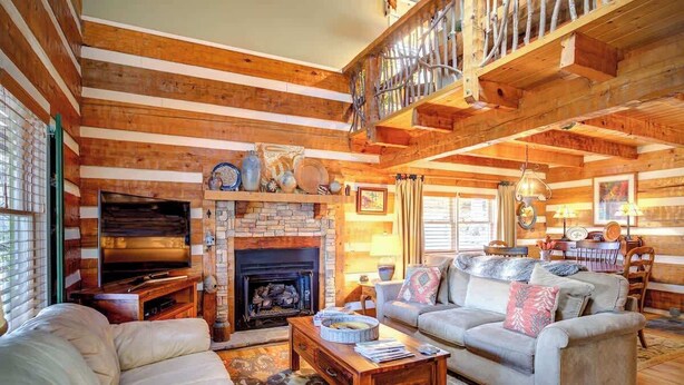 A log cabin interior with a fireplace, wooden walls, a sofa, and a dining area. - 3 Bedroom 3 Bath Log Cabin just outside of Blowing (Blowing Rock)