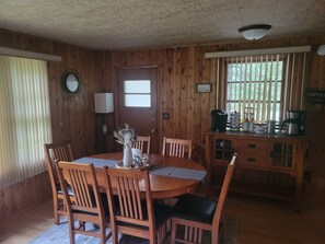 A wooden dining area with a round table, chairs, a vase with flowers, a coffee station with various coffee-making equipment, and a window with blinds. - Cozy 3-bedroom cabin in serene Park Rapids (Park Rapids)