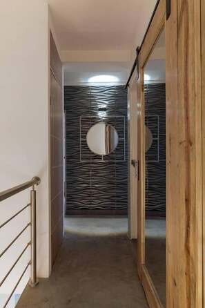 Ein Korridor mit Metallgeländer, einer Holztür und einer Wand mit geometrischem Muster.