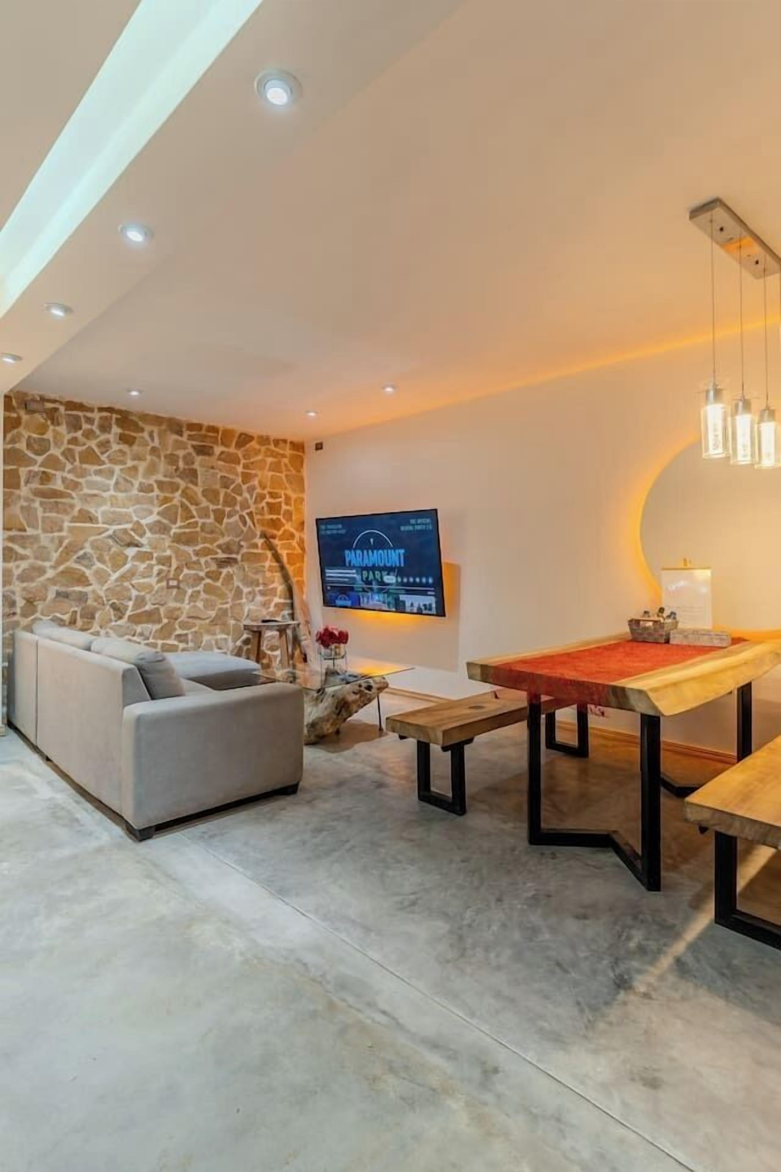 Un salon moderne avec un mur d’accent en pierre, un téléviseur à écran plat, une table de billard et un canapé.