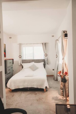 A bedroom with a bed, a dresser, a window with curtains, and a vase with flowers. - Luxury Home 2_Starlink 400 Mbit_AC_Jacuzzi_6 People (San Juan del Obispo)