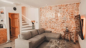 A modern living room with a stone wall, a sofa, a glass coffee table, and a wooden staircase. - Luxury Home 2_Starlink 400 Mbit_AC_Jacuzzi_6 People (San Juan del Obispo)