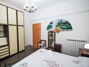 A hotel room with a bed, a chair, a wooden cabinet, a mirror, a fan, and a chandelier. - La Casa di Tea by Interhome (Borzonasca)