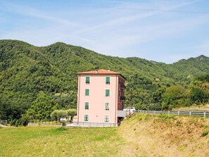 A pink building with multiple windows, situated on a hillside with a backdrop of green mountains. - La Casa di Tea by Interhome (Borzonasca)