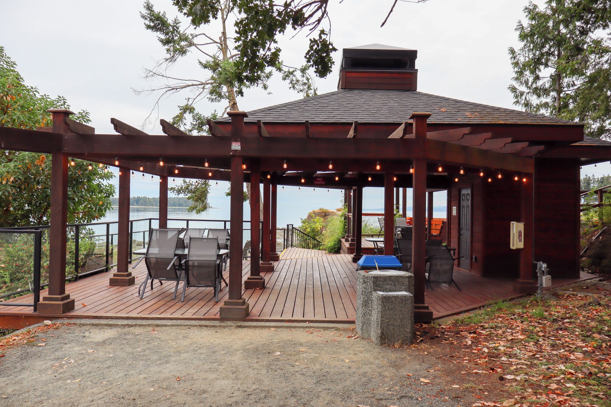 A covered outdoor seating area with tables and chairs, overlooking a body of water.