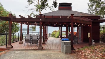 A covered outdoor seating area with tables and chairs, overlooking a body of water.