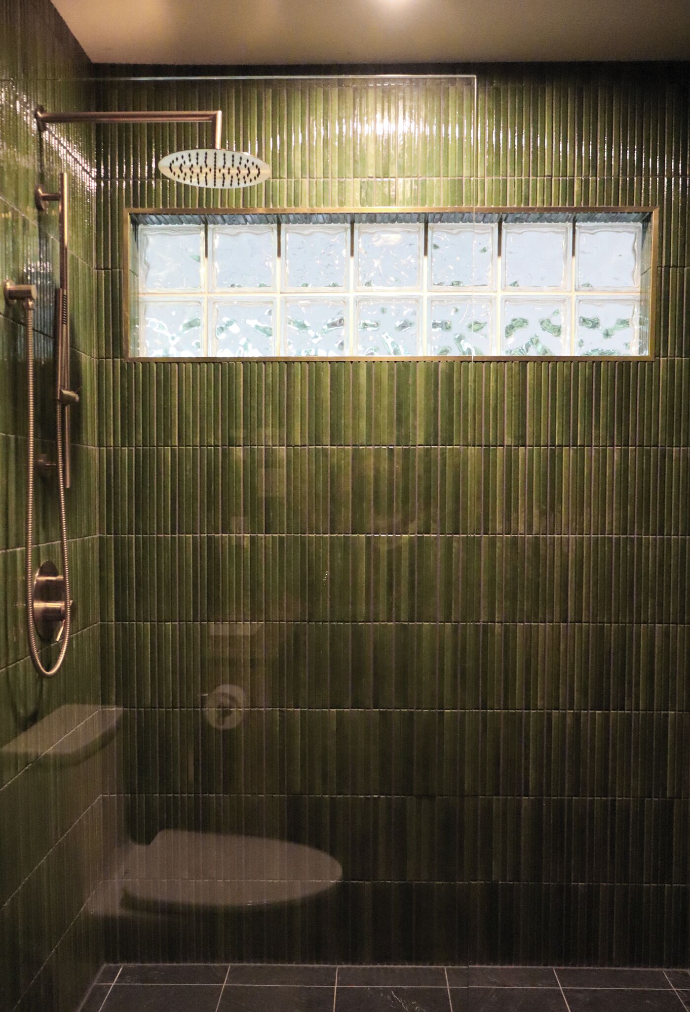 Une salle de bain avec un mur recouvert de carreaux verts, une fenêtre à verre dépoli et un espace douche.