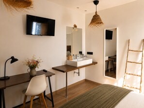 A modern bedroom with a bed, a desk, a chair, a TV, a large mirror, and a hanging light fixture.