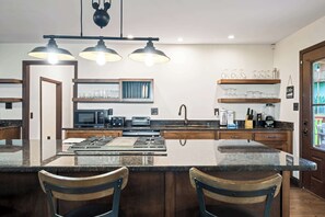 A modern kitchen with a central island, built-in appliances, and bar seating. - Maplecrest Retreat | Firepit • Hot Tub • Game Room (Sevierville)