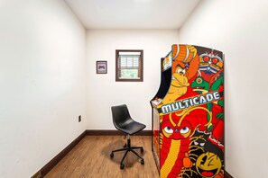 Ein Zimmer mit Holzboden, einem schwarzen Bürostuhl, einem Fenster mit Jalousien und einer farbenfrohen Spieluhr.